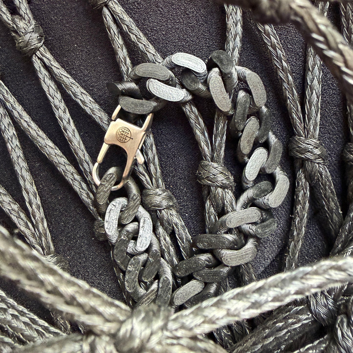 SeaChain Bracenet in 3D Druck aus alten Fischernetzen hergestellt in Schwarz mit kleinem Clip Karabiner in Silber liegt auf Fischernetzen.