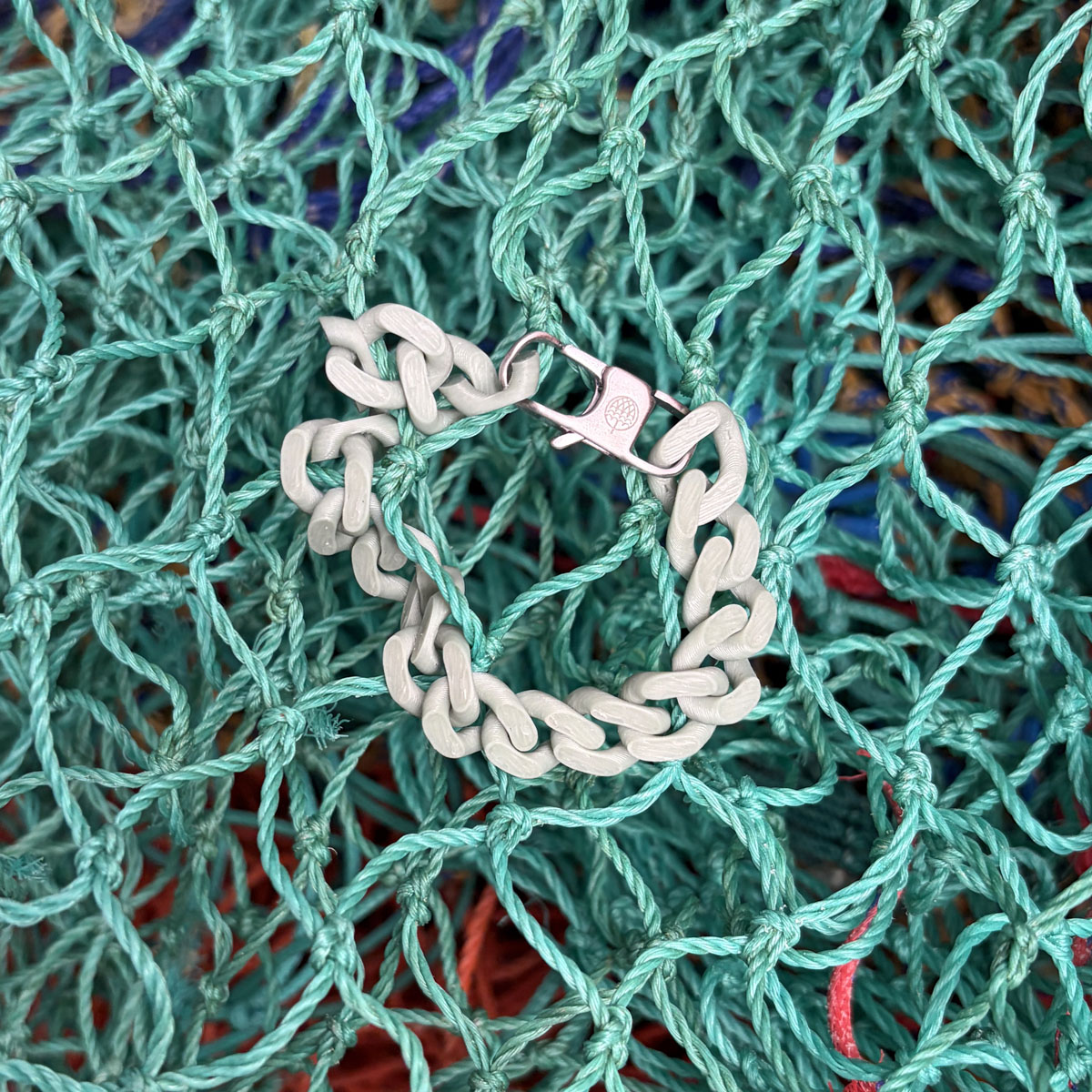 SeaChain Bracenet in 3D Druck aus alten Fischernetzen hergestellt in Blassgrün mit kleinem Clip Karabiner in Silber liegt auf Fischernetzen.