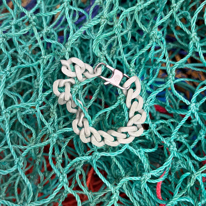 SeaChain Bracenet in 3D Druck aus alten Fischernetzen hergestellt in Blassgrün mit kleinem Clip Karabiner in Silber liegt auf Fischernetzen.