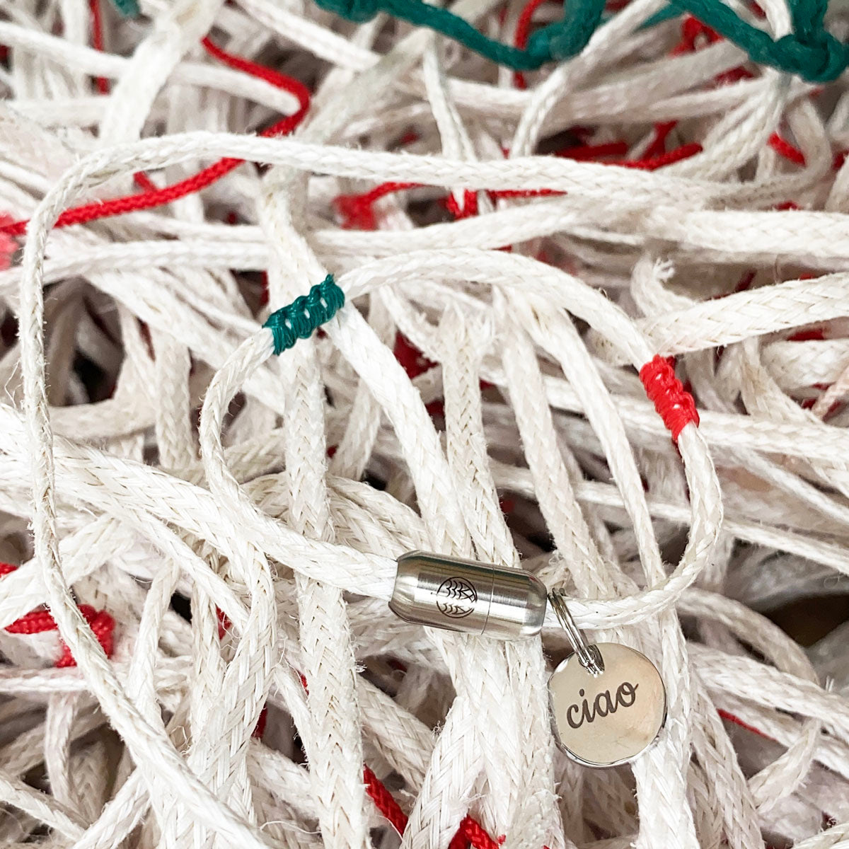 Italy, Italien Bracenet Bracelet  aus ehemaligem Fischernetz in Weiß mit roten und grünen Akzenten mit Edelstahl Magnetverschluss und einem Edelstahlanhänger mit Ciao Gravur mit Fischernetzen im Hintergrund