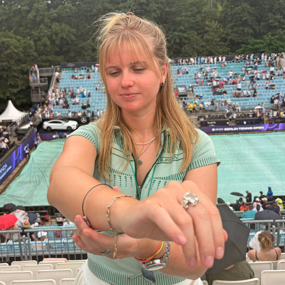 Person trägt CourtNet Armband aus Tennissaiten in Schwarz mit Drehverschluss in Silber am Handgelenk und steht an einem Tennisplatz