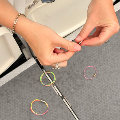 CourtNet Armband aus Tennissaiten in Pink mit Drehverschluss in Roségoldauf dem Boden. Eine Person dreht den Drehverschluss in Silber zu. 