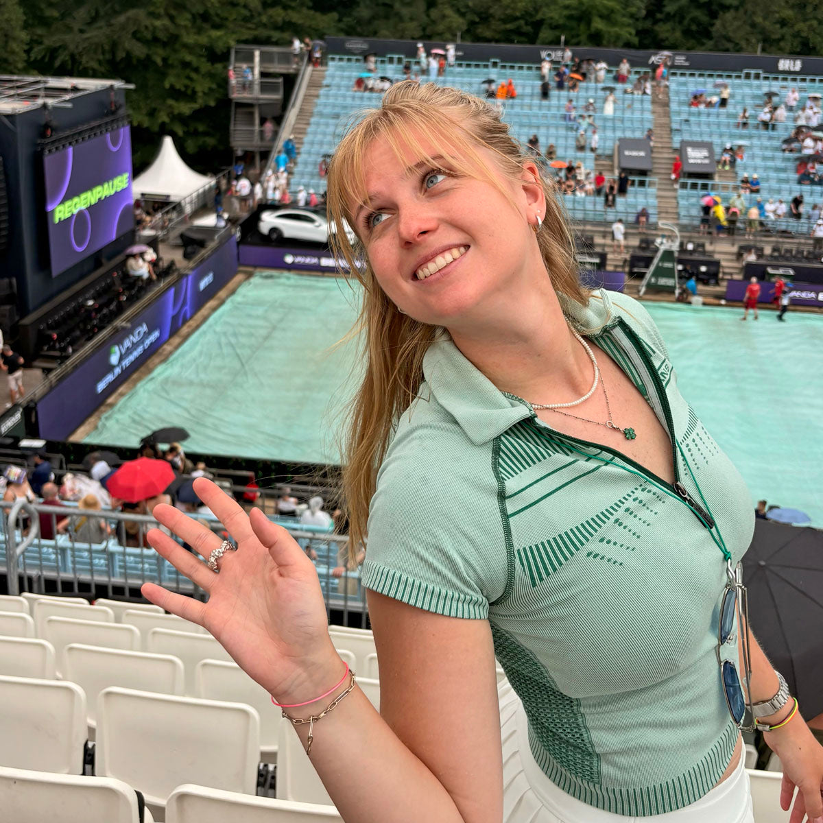Person trägt das CourtNet Armband aus Tennissaiten in Pink mit Drehverschluss in Roségold am Handgelenk und steht an einem Tennisplatz