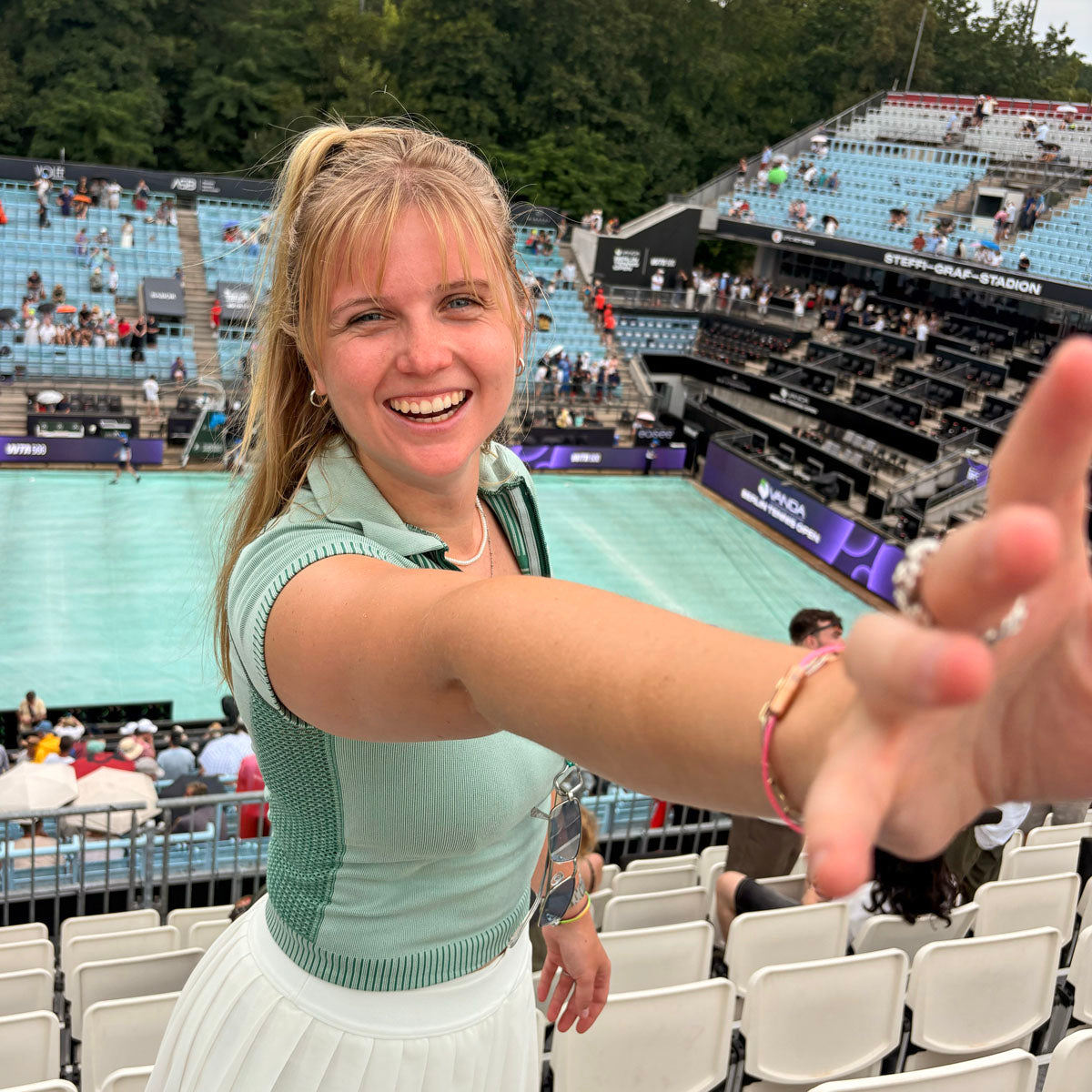 Person steht am Tennisplatz und trägt ein CourtNet Armband aus Tennissaiten in Pink mit Drehverschluss in Roségold am Handgelenk