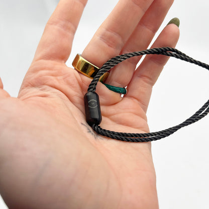 Person hält das Sea Shepherd X BRACENET x humanvoll Armband aus schwarzen Fischernetzen mit schwarzem Magnetverschluss auf dem das Sea Shepherd Logo, das humanvoll Logo und das BRACENET Logo graviert sind in der Hand