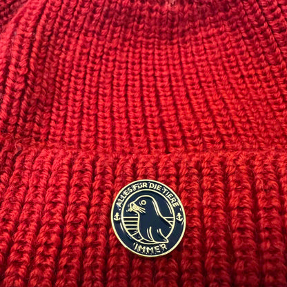 "Alles für die Tiere" Ansteck-Pin aus Emaille in Blau und Gold mit "Alles für die Tiere, immer" Schriftaufzug, sowie Robben-Motiv ist an einer Mütze angebracht.