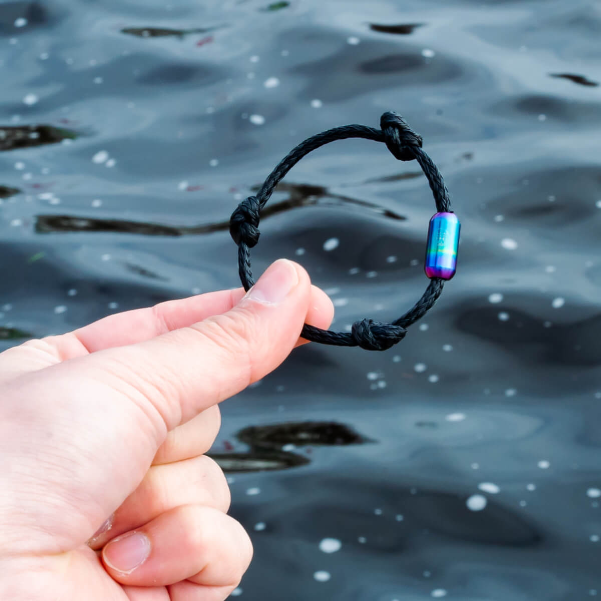 Person hält das BRACENET Armband Black Sea II mit buntem Magnetverschluss, im Hintergrund die Alster