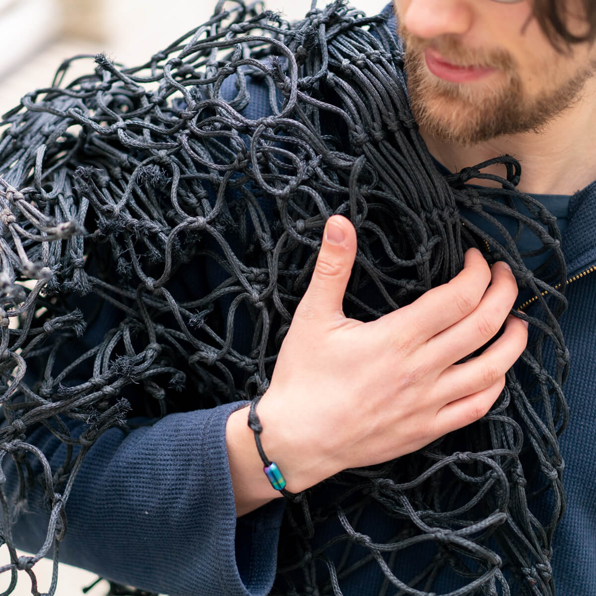 Person trägt das alte Fischernetz in schwarz über die Schulter und trägt dabei das handgefertigte Upcycling Armband von BRACENET