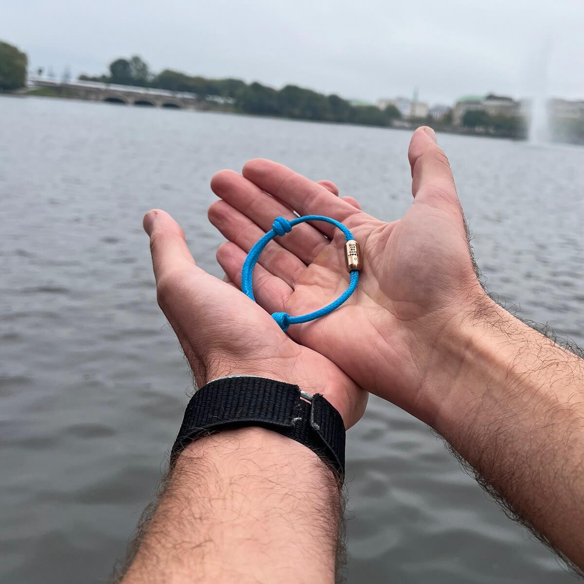 Person steht an der Alster und hält das BRACENET Armband von Malte Zierden in den Händen