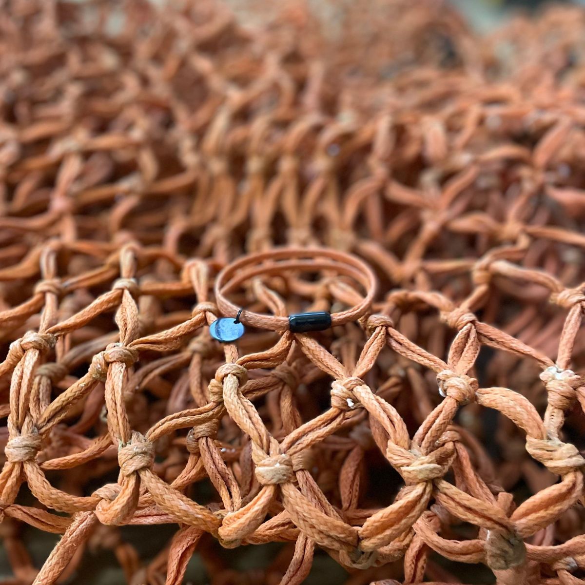 BRACENET Ghost Diving USA aus alten Fischernetzen in orange. Das Armband liegt auf dem Netz aus dem es gefertigt wurde. 