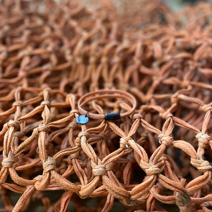 BRACENET Ghost Diving USA aus alten Fischernetzen in orange. Das Armband liegt auf dem Netz aus dem es gefertigt wurde. 