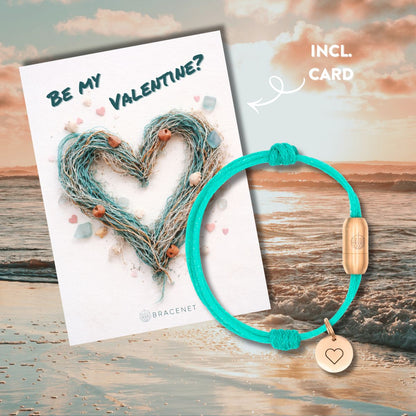 BRACENET Valentinstagsbundle mit einer Postkarte auf der ein Herz aus Fischernetzen abgebildet ist, sowie der Schriftzug "Be My Valentine?". Dazu gibt es ein Armband aus Bali Sea Fischernetz mit rosé Bajonettverschluss aus Edelstahl und einem rosé Edelstahlanhänger. Im Hintergrund sieht man einen Sonnenuntergang am Meer. 
