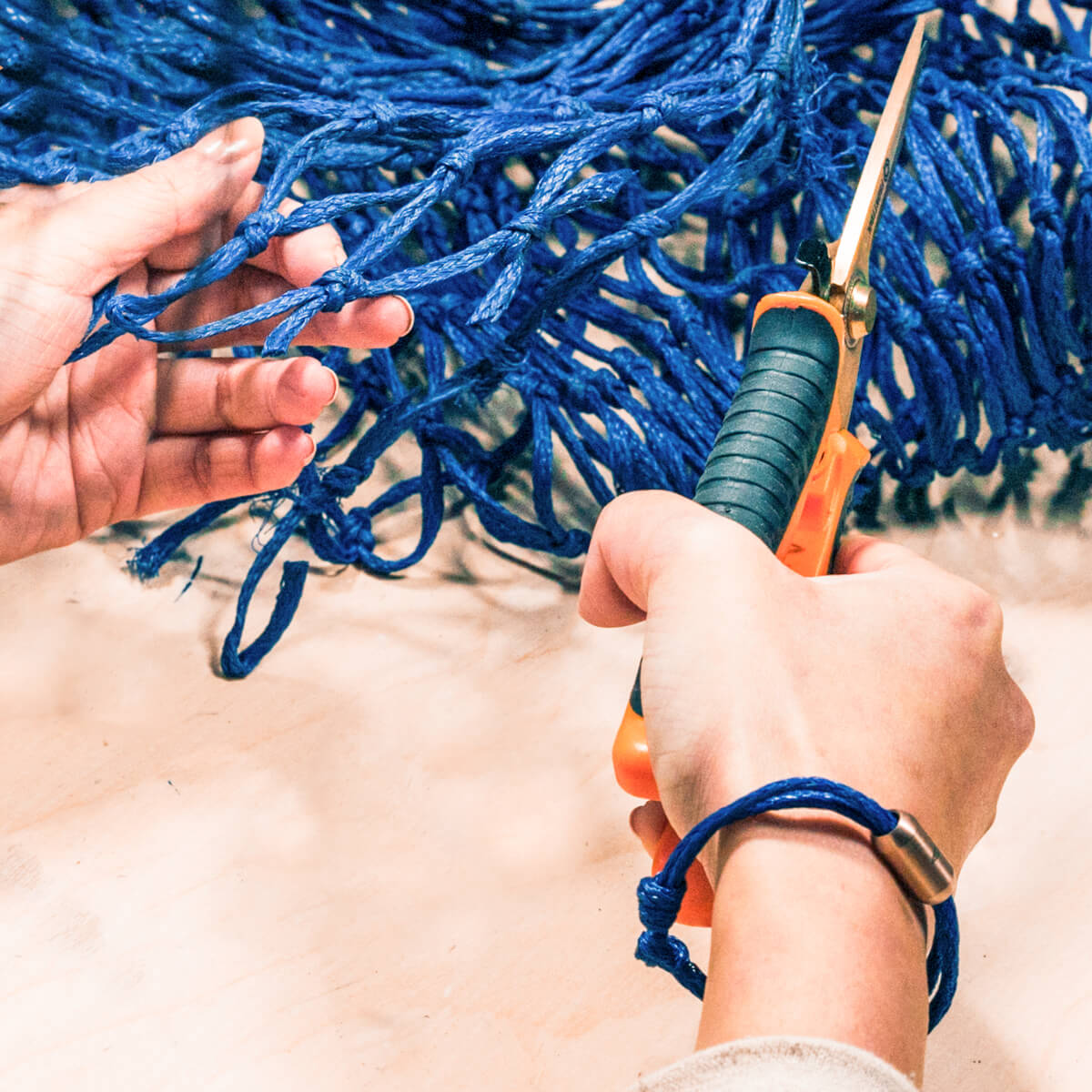 Person trägt das BRACENET Upcycling Armband Baffin Bay aus alten blauen Fischernetzen mit silberner Tube und fertigt per Handarbeit weitere Armbänder aus dem geborgenen Geisternetz.