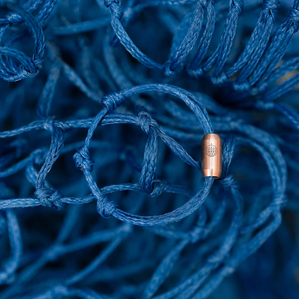 Das BRACENET Upcycling Armband Baffin Bay aus alten blauen Fischernetzen mit roségoldener Tube liegt auf dem geborgenen Geisternetz.