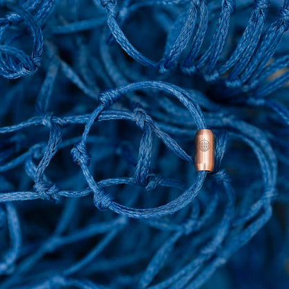 Das BRACENET Upcycling Armband Baffin Bay aus alten blauen Fischernetzen mit roségoldener Tube liegt auf dem geborgenen Geisternetz.