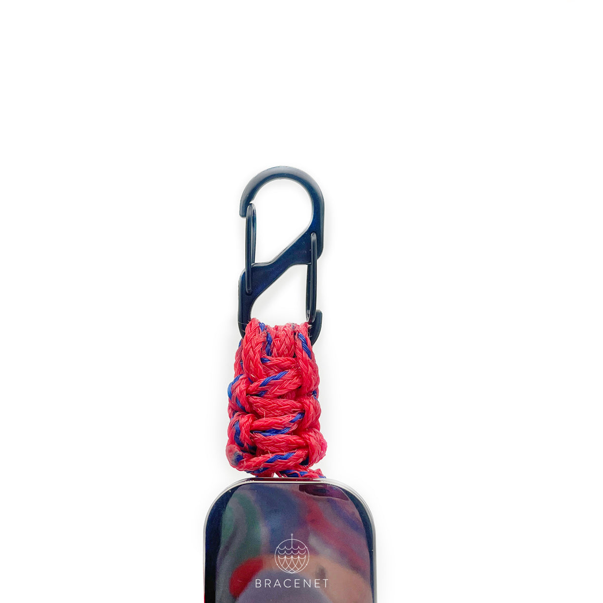 BRACENET Karten- und Schlüsselhalter mit ausziehbarer Zugrolle, BRACENET Logo, Schnürung aus Red Sea Fischernetz und schwarzem Karabiner in der Hand. Der Fokus liegt auf dem roten Makramee Knoten aus dem Red Sea Fischernetz.