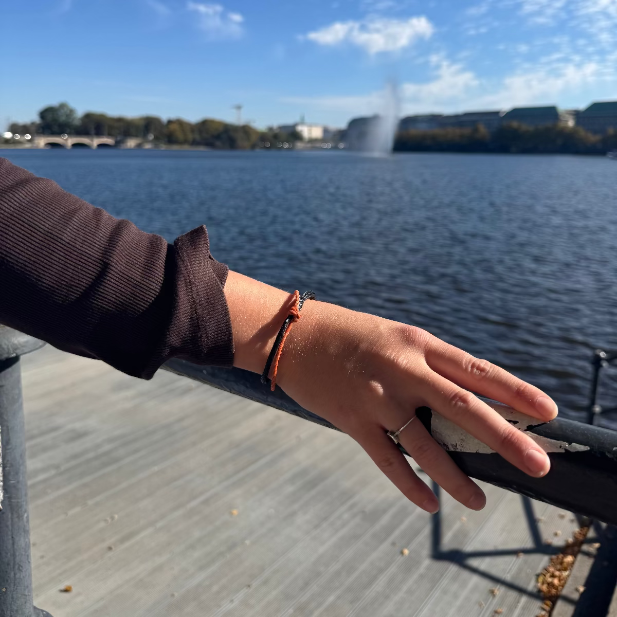 Person trägt das Oktober Bracenet Cardigan Bay aus einem Strang Fischernetz in Schwarz und einem Strang Fischernetz in Orange, verbunden mit einem Knoten und einem Magnetverschluss in Schwarz am Handgelenk. 