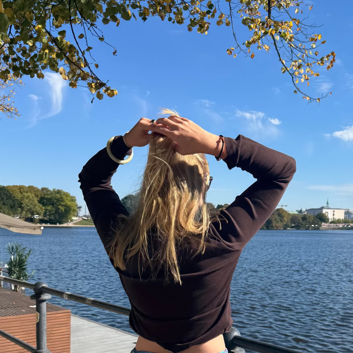 Person trägt das Oktober Bracenet Cardigan Bay aus einem Strang Fischernetz in Schwarz und einem Strang Fischernetz in Orange, verbunden mit einem Knoten und einem Magnetverschluss in Schwarz am Handgelenk und macht sich die Haare. 