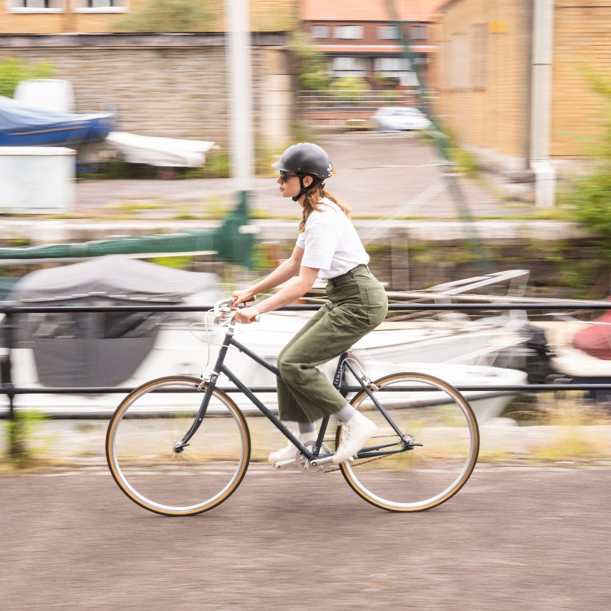 Person trägt Dashel x BRACENET Sea Shepherd Fahrradhelm in Schwarz mit Fischernetz-Schlaufe in Gelb und Blau und fährt mit dem Fahrrad. 