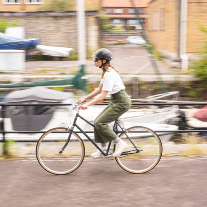 Person trägt Dashel x BRACENET Sea Shepherd Fahrradhelm in Schwarz mit Fischernetz-Schlaufe in Gelb und Blau und fährt mit dem Fahrrad. 