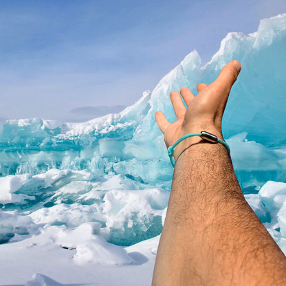 Person trägt das BRACENET Upcycling Armband Glacier Bay aus eisblauen Fischernetzen und 2 Knoten mit silbernen Bajonettverschluss am Handgelenk, im Hintergrund eisblaue Gletscher