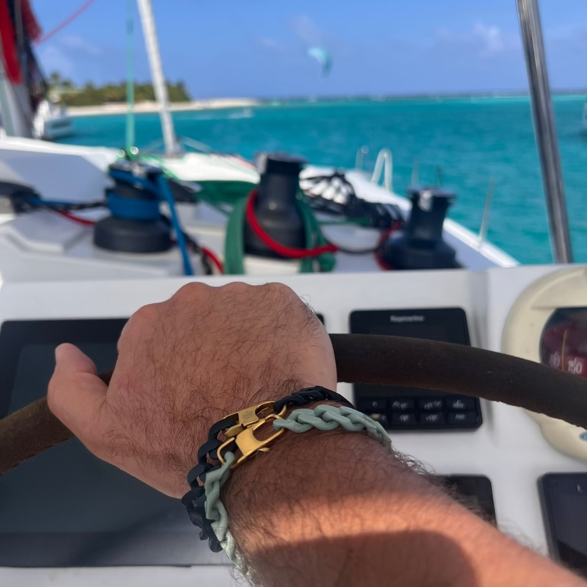 Person trägt zwei SeaChain Bracenet in 3D Druck aus alten Fischernetzen hergestellt in Blassgrün und Schwarz mit kleinem Clip Karabiner in Gold und Silber am Handgelenk und lenkt ein Boot