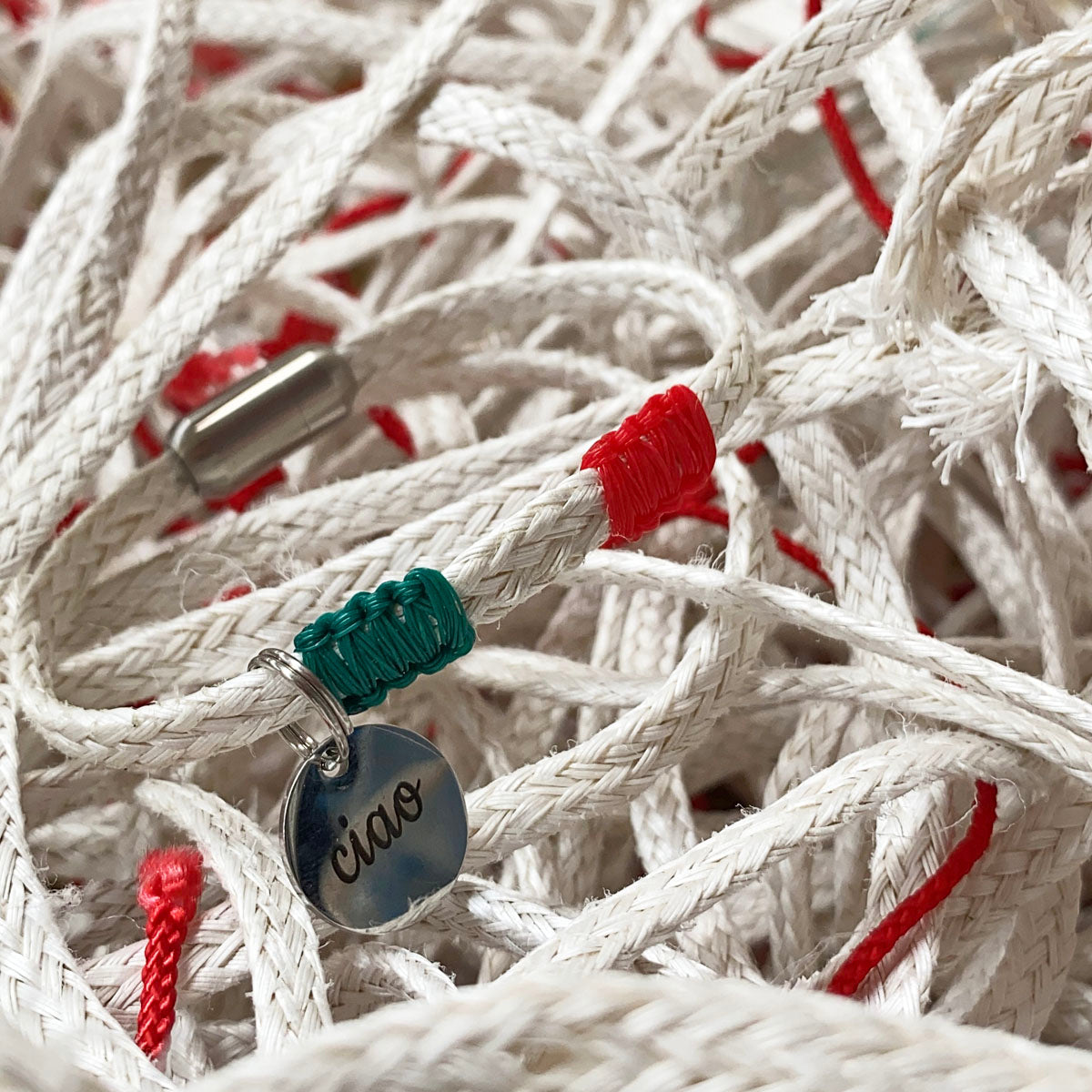 Italy, Italien Bracenet Bracelet  aus ehemaligem Fischernetz in Weiß mit roten und grünen Akzenten mit Edelstahl Magnetverschluss und einem Edelstahlanhänger mit Ciao Gravur mit Fischernetzen im Hintergrund