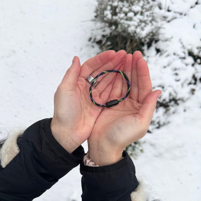 Person hält das Januar Bracenet Kara Sea aus schwarzem Fischernetz mit Umwicklungen aus Dolly Ropes in Grün und Lila mit schwarzem Bajonettverschluss in den Händen über dem Schnee. 