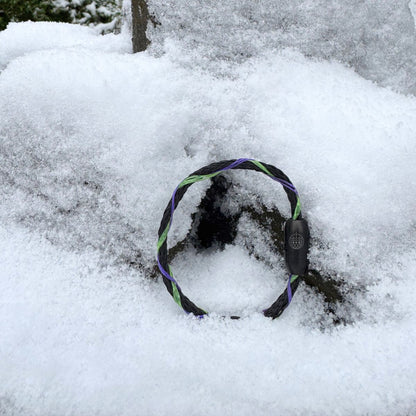 Das Januar Bracenet Kara Sea aus schwarzem Fischernetz mit Umwicklungen aus Dolly Ropes in Grün und Lila mit schwarzem Bajonettverschluss steht im Schnee an einen Stein gelehnt. 