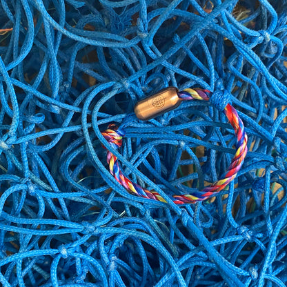 Kids' Bracenet Lübecker Bucht aus einem Strang blauem Fischernetz und einem Strang buntem Fischernetz, größenverstellbar mit Magnetverschluss in Roségold liegt auf Fischernetzen. 