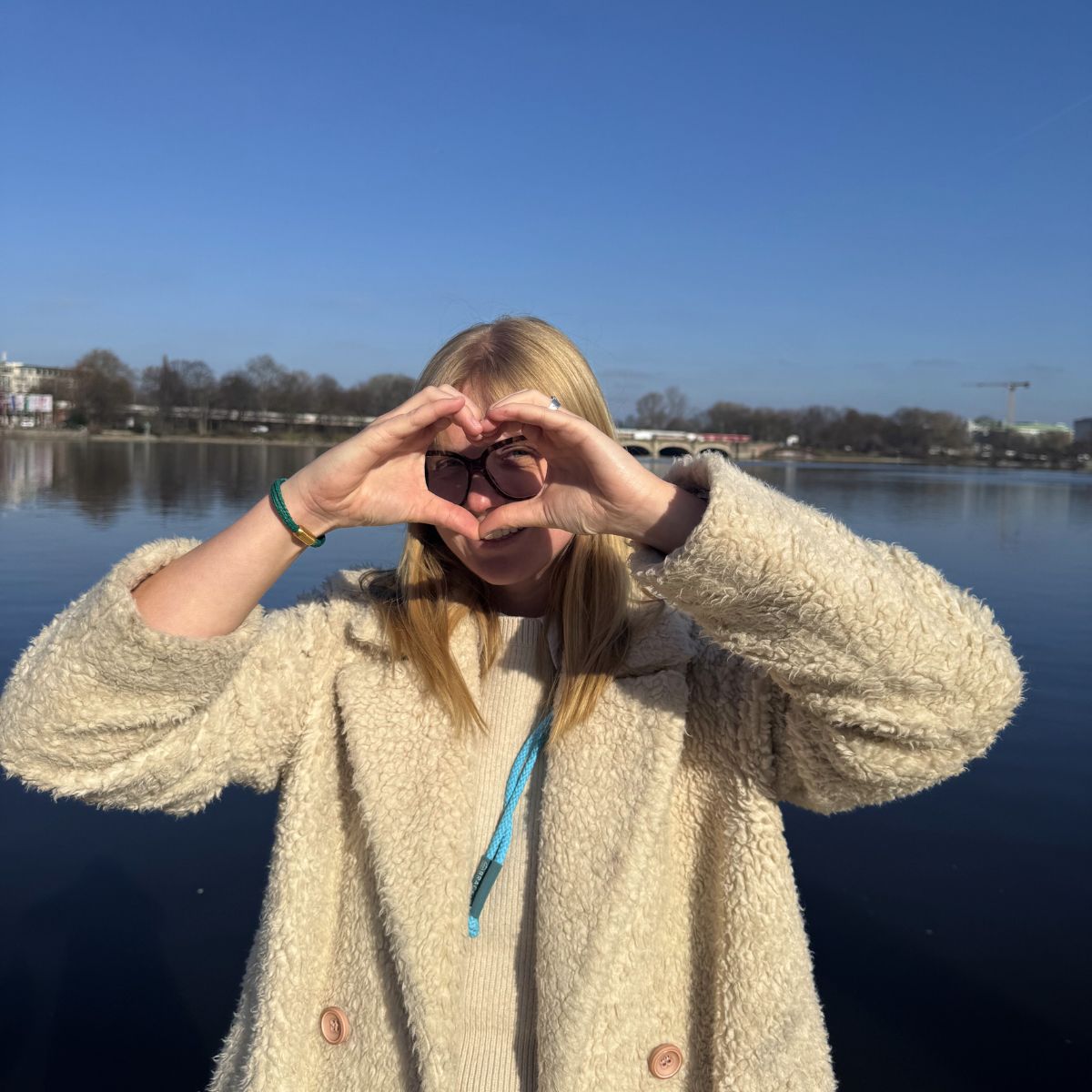 Person trägt das März Bracenet Alborán Sea aus dunkelgrünem Fischernetz mit Knoten und mit goldenem Magnetverschluss am Handegelenk und formt mit den Händen ein Herz vor dem Gesicht.