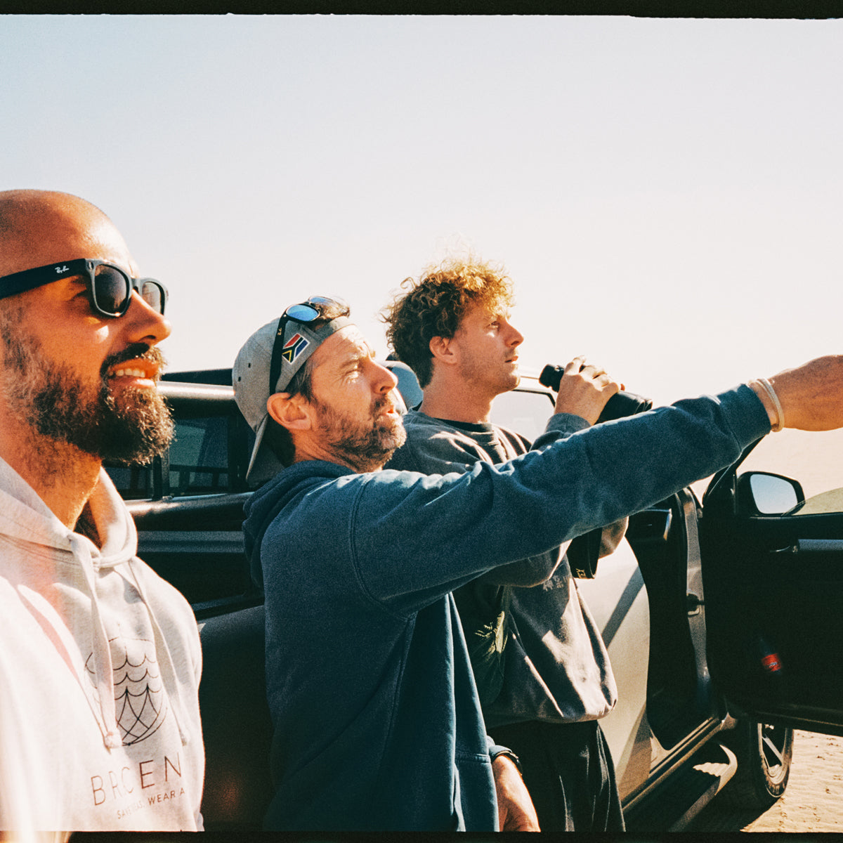 Malte Zierden und Benjamin von BRACENET stehen mit einer weiteren Person vor einem Auto und beobachten die Robben mit einem Fernglas.