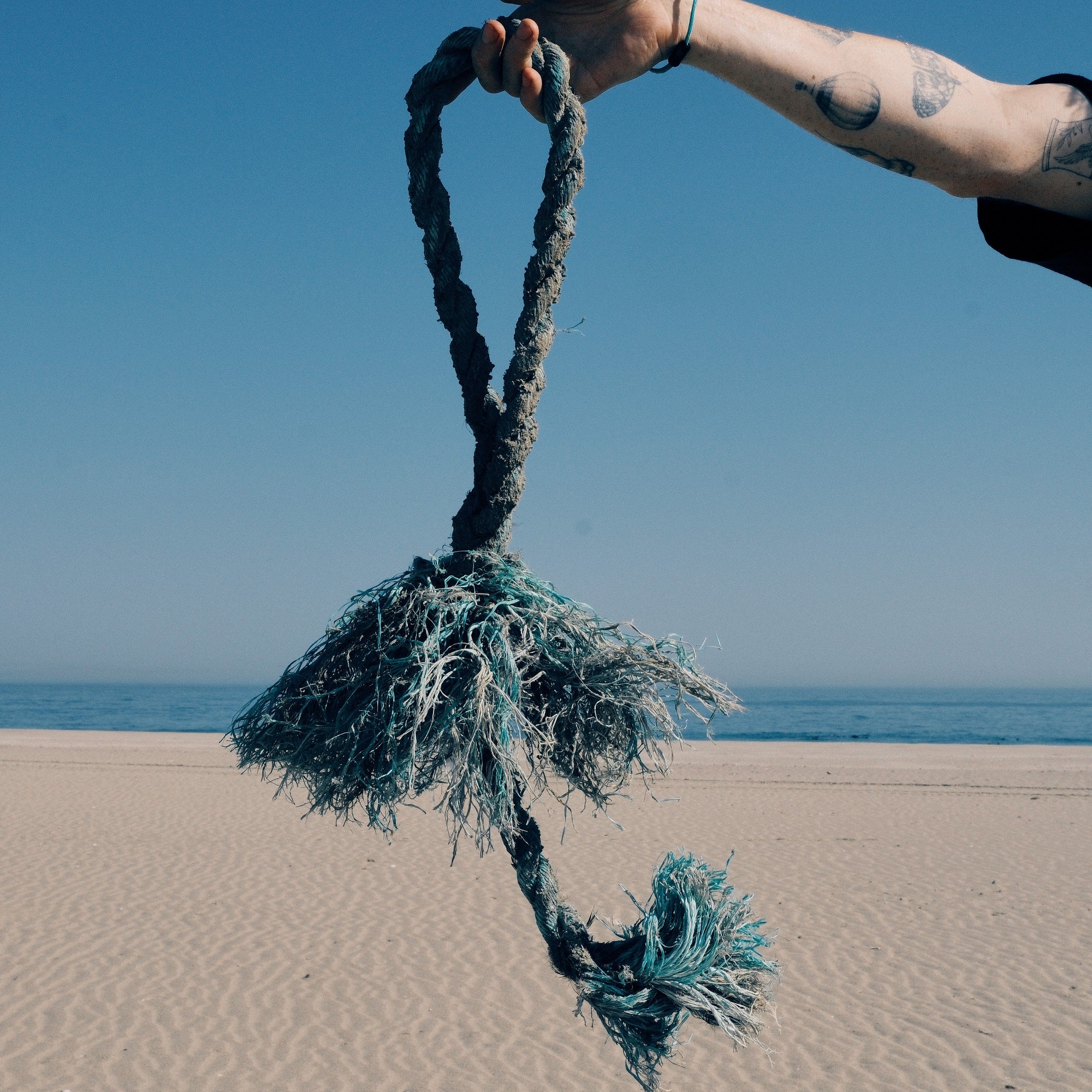 Ein altes Fischereiseil in blau wird von einer Person hochgehalten, im Hintergrund ein langer Sandstrand in Namibia