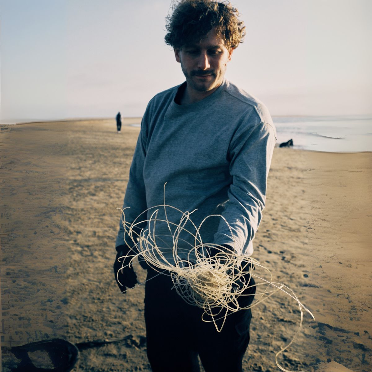 Malte Zierden steht am Strand in Namibia und zeigt die Angelschnüre, die er von einer Robbe befreit hat, im Hintergrund das Meer
