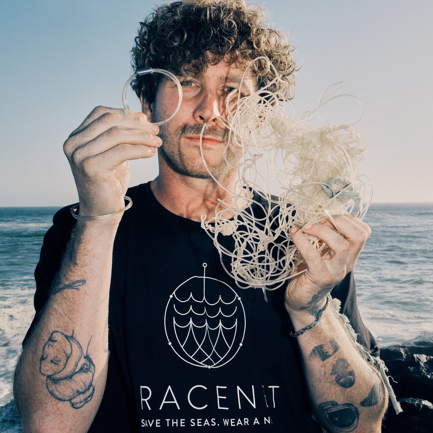 Der Tierschützer Malte Zierden steht am Strand von Namibia und hält in einer Hand geborgene Angelschnur und in der anderen Hand ein Armband daraus, im Hintergrund das Meer