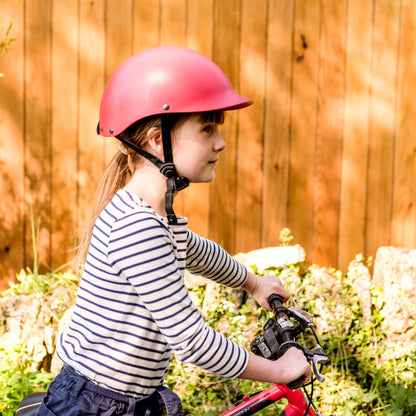 Mädchen trägt Dashel x BRACENET Kids' Ocean Fahrradhelm in Rot mit Schlaufe aus Fischernetzen in Gelb und Blau. 