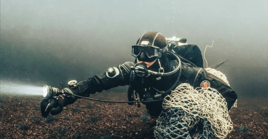 Taucher schwimmt auf Meeregrund und trägt ein Geisternetz