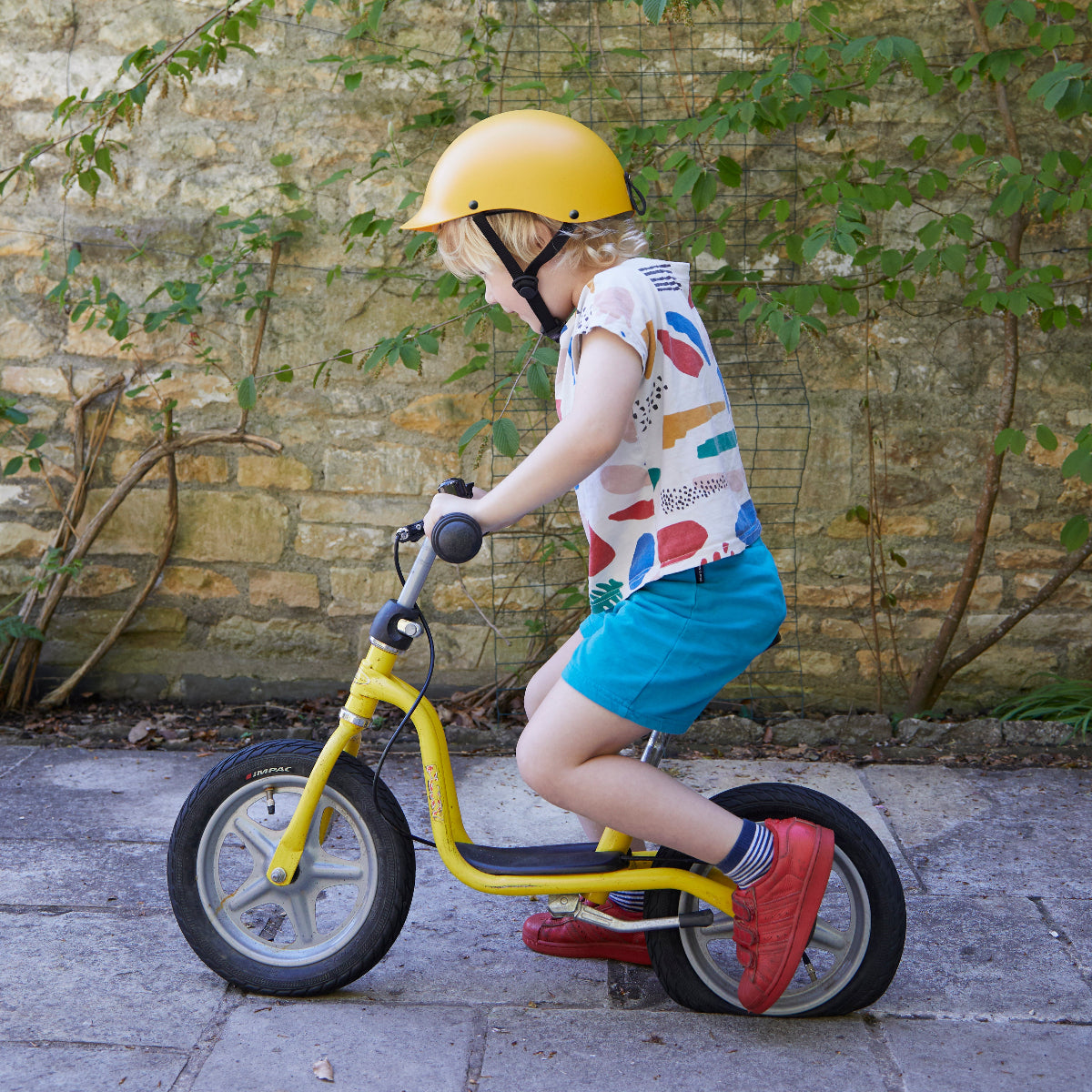 Junge trägt Dashel x BRACENET Kids' Ocean Fahrradhelm in Gelb mit Schlaufe aus Fischernetzen in Gelb und Blau und fährt Fahrrad.