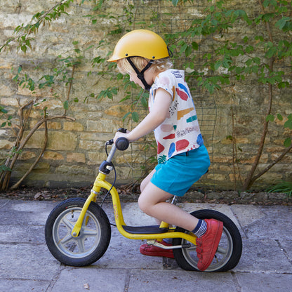 Junge trägt Dashel x BRACENET Kids' Ocean Fahrradhelm in Gelb mit Schlaufe aus Fischernetzen in Gelb und Blau und fährt Fahrrad.