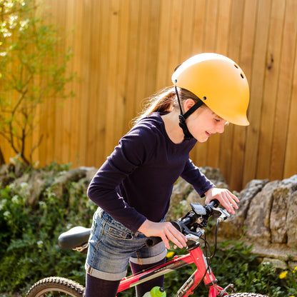 Mädchen trägt Dashel x BRACENET Kids' Ocean Fahrradhelm in Gelb mit Schlaufe aus Fischernetzen in Gelb und Blau und steht mit einem Fahrrad.