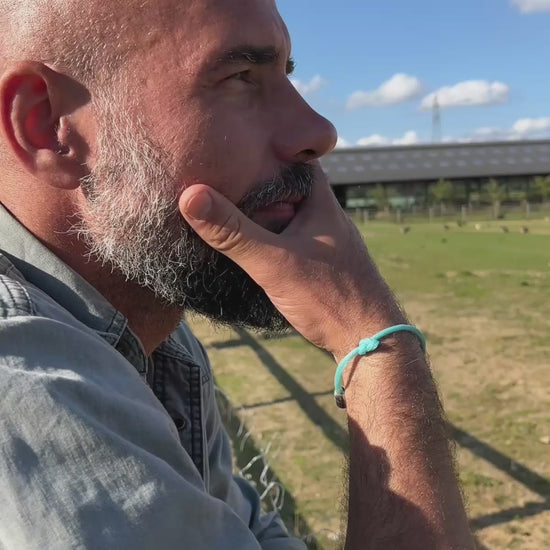 Video von Person, die das BRACENET Upcycling Armband Glacier Bay aus eisblauen Fischernetzen und 2 Knoten mit silbernen Bajonettverschluss am Handgelenk trägt und in die Ferne schaut