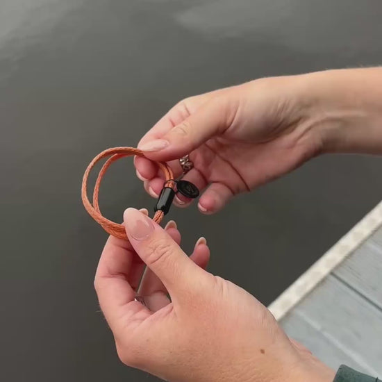 Produktvideo von einer Person, die das BRACENET Upcycling Armband Ghost Diving USA aus orangenen alten Fischernetzen und einem schwarzen Magnetverschluss und Edelstahlanhänger ans Handgelenk anlegt