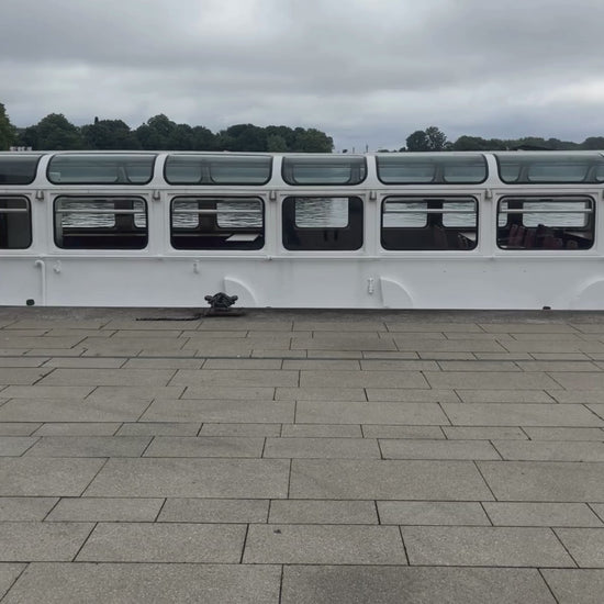 Person läuft in dem video durch das Bild und trägt eine graue Tasche an der der BRACENET Upcycling Taschenanhänger Flores Sea aus blauen alten Fischernetzen mit einem silber Edelstahlanhänger mit BRACENET Logo und einem silber Edelstahlclip in Herzform befestigt ist. 