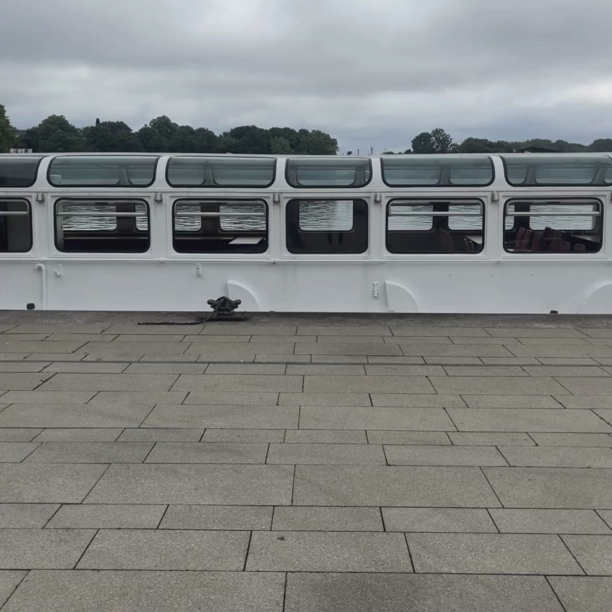 Person läuft in dem video durch das Bild und trägt eine graue Tasche an der der BRACENET Upcycling Taschenanhänger Flores Sea aus blauen alten Fischernetzen mit einem silber Edelstahlanhänger mit BRACENET Logo und einem silber Edelstahlclip in Herzform befestigt ist. 