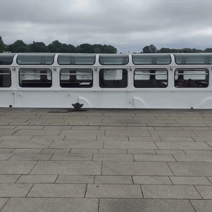 Person läuft in dem video durch das Bild und trägt eine graue Tasche an der der BRACENET Upcycling Taschenanhänger Flores Sea aus blauen alten Fischernetzen mit einem silber Edelstahlanhänger mit BRACENET Logo und einem silber Edelstahlclip in Herzform befestigt ist. 